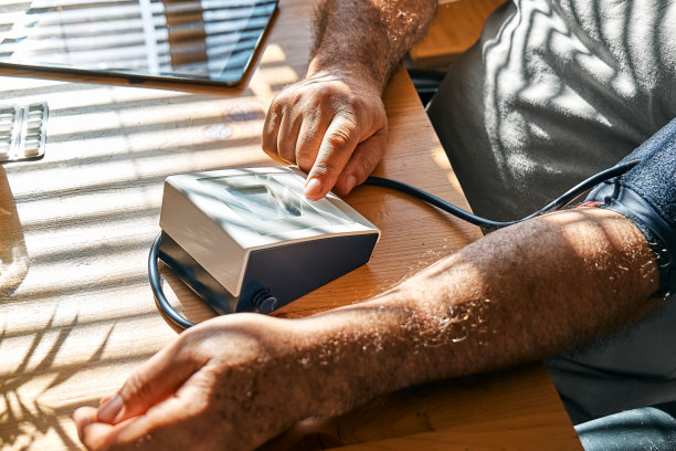 一名中年男子早上测量自己的动脉血压，在家用血压袖带检查自己的健康状况。高血压或低血压问题的概念。图片下载