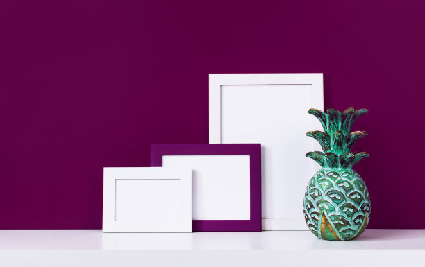 一个木制的空相框，一个木制的祖母绿菠萝放在一个白色的架子上，背景是明亮的紫红色墙壁。空白纸框架，现代家居装饰模型。室内背景。图片下载