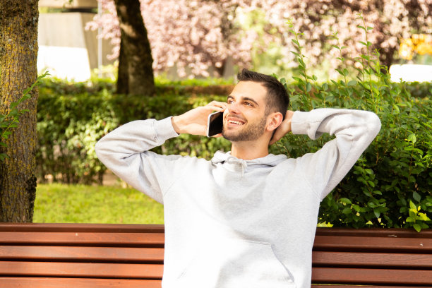 有胡子有手机的迷人年轻人坐在公园里图片下载