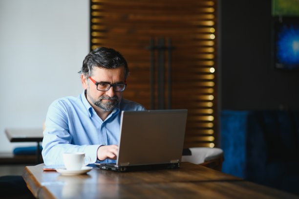 高级男性自由职业者在咖啡馆的笔记本电脑上工作。远程工作的概念。图片下载