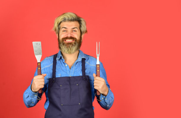 烧烤食物。烹饪用具。夏季野餐。烧烤是美国传统。烹饪概念。工具烤肉。穿着围裙的男人拿着烧烤架。潮人染胡子推广烧烤设备。烹饪健康图片下载