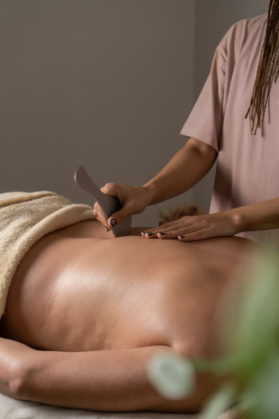 在舒适的办公室里，按摩师用金属按摩工具给躺在沙发上的女人做背部按摩。健康理念，身体护理，护肤，养生。垂直图图片下载