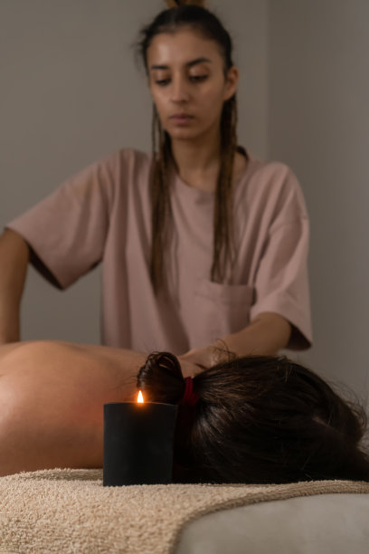 按摩师在办公室的沙发上为女士按摩颈部，焦点在蜡烛上。健康和身体护理概念。竖版照片图片下载
