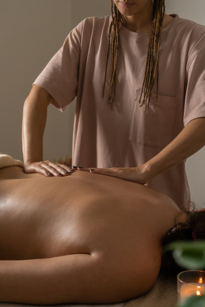 按摩师在舒适的水疗沙龙的绿色植物，燃烧的蜡烛做背部按摩。健康的生活方式和身体护理的理念。垂直图图片下载