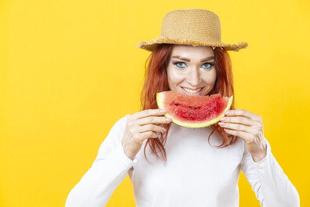 一个可爱的白人漂亮的年轻女子在草帽与多汁西瓜的颜色背景。图片下载