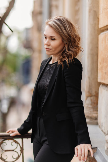 一个穿着黑色西装的美丽自信的女人站在老建筑的阳台上。图片下载