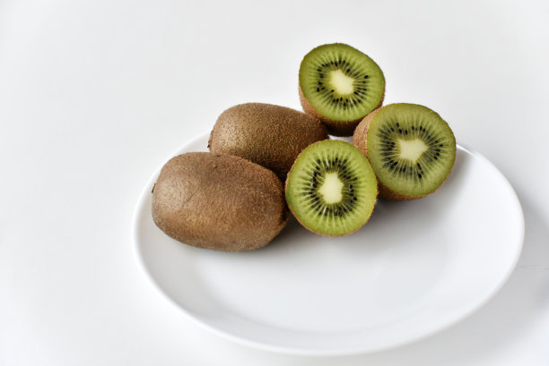 一个完整的猕猴桃和一半放在一个白色的盘子里图片下载