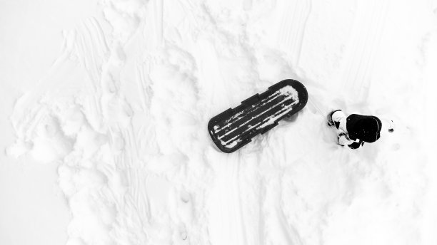 高空无人机拍摄的一个孩子用雪橇爬上积雪覆盖的小山的照片。图片下载