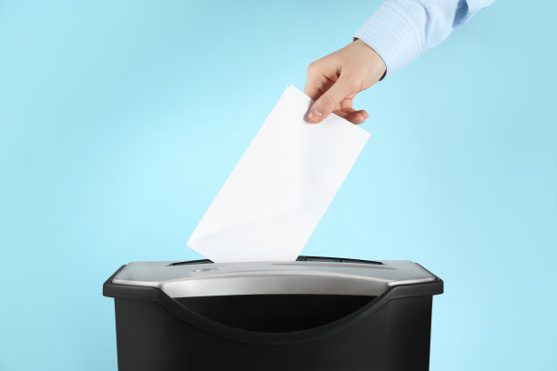 一名女子在浅蓝色背景上用碎纸机破坏信封，特写图片下载