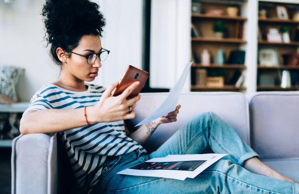 专注的少数民族女性在家中使用智能手机处理图表图片下载