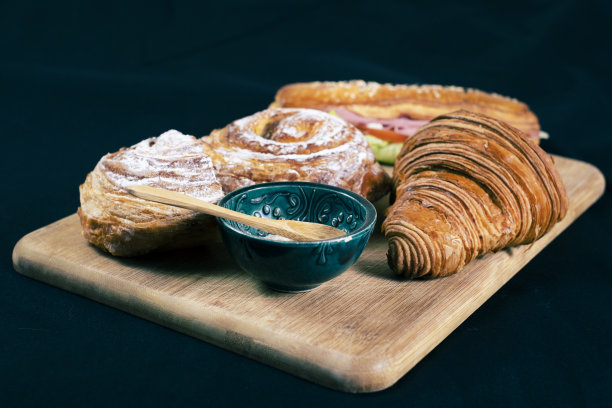 黑色背景的欧式早餐。木制案板上有牛角面包和三明治。Pain aux raisins，也叫escargot或Pain russe，是一种带有奶油和葡萄干的螺旋状糕点。图片下载