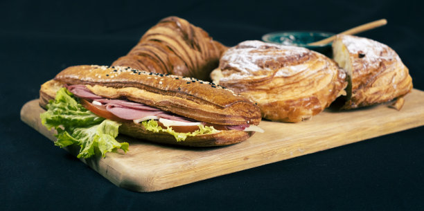 黑色背景的欧式早餐。木制案板上有牛角面包和三明治。Pain aux raisins，也叫escargot或Pain russe，是一种带有奶油和葡萄干的螺旋状糕点。图片下载