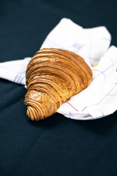 黑色背景的欧式早餐。木制案板上有一个加了糖粉的羊角包。图片下载