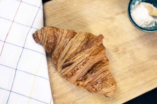 黑色背景的欧式早餐。木制案板上有一个加了糖粉的羊角包。图片下载