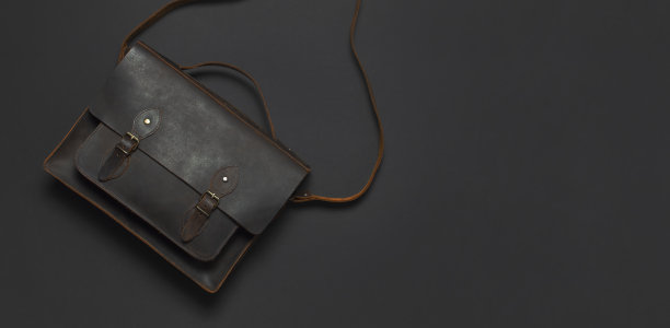 时尚的概念。棕色皮革男士包在黑色背景顶部视图平铺与复制空间。办公公文包，商务配件，时尚男装，商务背景。图片下载