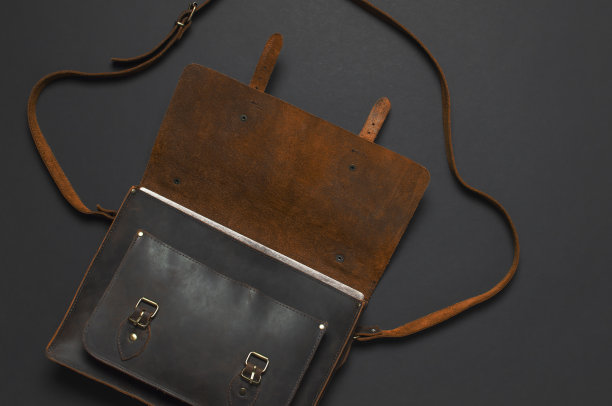 时尚的概念。棕色皮革男士包在黑色背景顶部视图平铺与复制空间。办公公文包，商务配件，时尚男装，商务背景。图片下载
