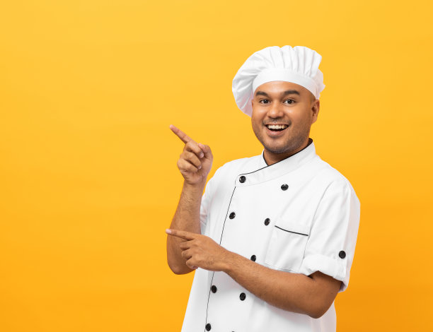 微笑年轻英俊的亚洲男子厨师在制服与帽子站立指着手指在黄色背景空白的文字。厨师职业厨师或面包师在厨房、餐厅和酒店工作的人。图片下载