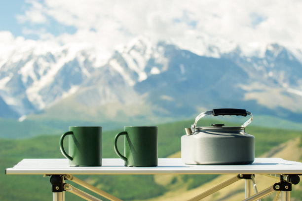 茶壶和马克杯放在游客桌上，背景是群山。户外休闲旅游登山休息。图片下载