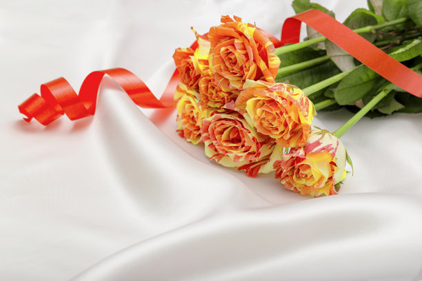 白色缎子床单上的一束彩色玫瑰花。爱情和浪漫的主题。情人节概念。美丽的花卉背景图片下载