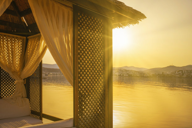 夕阳西下，地平线上明亮的阳光洒在水面上，照亮了海滩上的木制凉亭图片下载