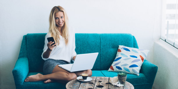 成功的女性自由职业者在舒适的沙发上休息，使用现代智能手机和笔记本电脑技术在家庭内部做远程工作，开朗的潮女孩连接到蓝牙图片下载