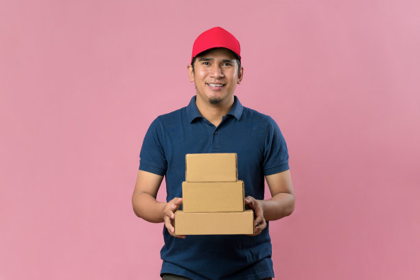 快乐的年轻送货员在红帽子拿着包裹邮筒图片下载