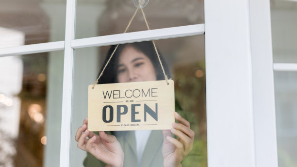 女店主透过门玻璃打开招牌，准备为顾客服务。小生意的女老板为重新开业转动牌子图片下载