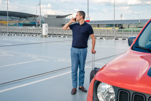 一个拿着行李的人在停车场讲电话。图片下载