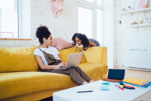 黑人妇女在笔记本电脑上工作，女儿露出舌头图片下载