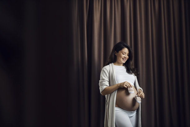 怀孕快乐的女人正在期待宝宝和抱着婴儿鞋。图片下载