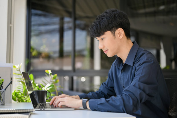 专业的亚洲商人使用笔记本电脑，在他的办公桌上的笔记本键盘上打字。图片下载