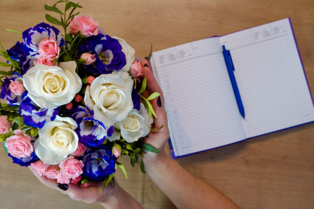 Flatlay。女性手中捧着一束五彩缤纷的玫瑰花。笔记本、日记本和一支笔放在木桌上图片下载