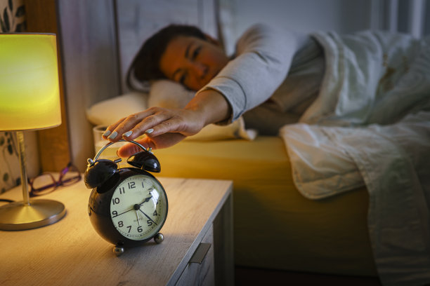 躺在床上的女人从床头柜上拿起闹钟图片下载