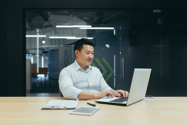 一位亚洲老师坐在桌旁。他使用笔记本电脑工作，远程在线授课图片下载