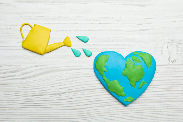 地球日快乐。在白色的木桌上，用橡皮泥行星和洒水罐平铺构图图片下载
