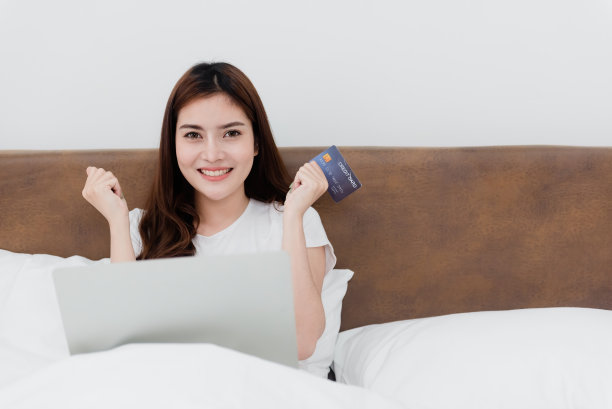 亚洲美女用信用卡通过互联网用电脑购物带着快乐的笑脸，成为网上商务在家购物体验的新常态。图片下载