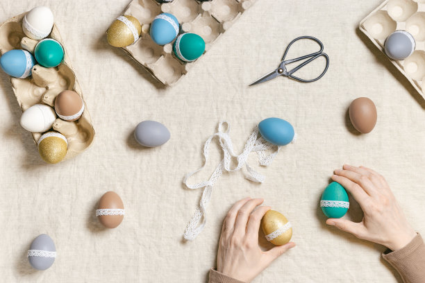 装饰彩色彩蛋，准备快乐的复活节庆祝活动，妇女装饰染色鸡蛋与胶带花边在桌布生活方式美学照片在家里，diy节日图片下载