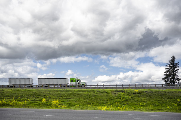 经典的绿色强大的美国大卡车在两个散装半挂车的运输货物行驶在山顶的道路上图片下载