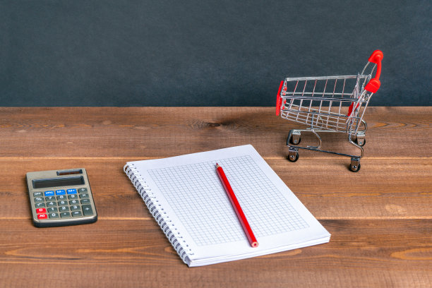 计划，预算，计算购物成本。计算器，记事本和购物车在木制的桌子上。图片下载