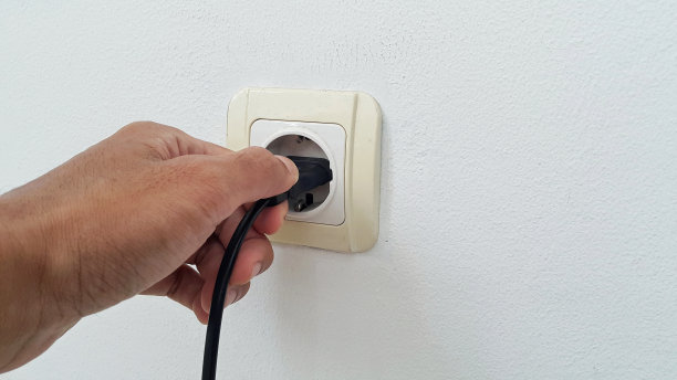 用手把电源线插到白墙上的白色塑料插座上图片下载