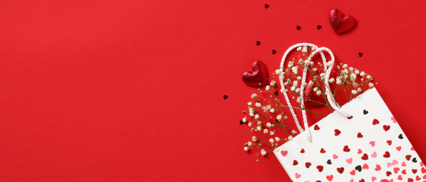 情人节快乐横幅模板。红色背景上有春天花朵和心形糖果的纸购物袋。图片下载