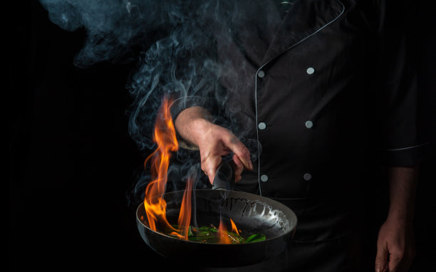 厨师在平底锅里烹饪食物，黑色背景上有火焰。餐厅及酒店服务理念。免费广告位图片下载