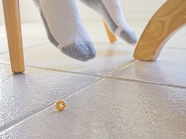 早餐麦片散落在厨房地板上，背景是孩子的脚、桌子和椅子图片下载