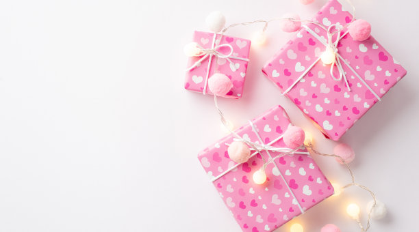 情人节的概念。顶部视图照片粉红色礼盒的包装纸与心形图案发光的花环和软绒球孤立的白色背景与复印空间图片下载