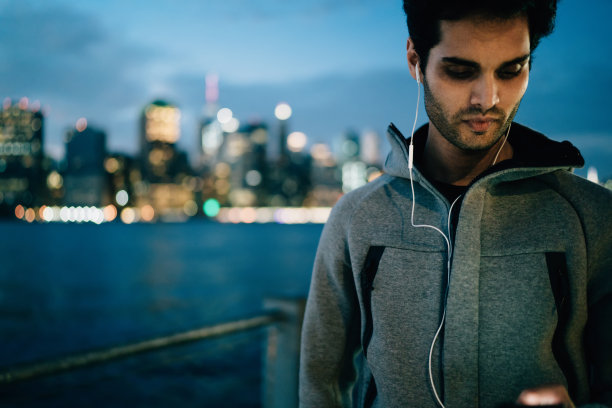 在纽约，健康男士使用智能手机上的4g无线连接在体育网站上搜索晚间训练练习，男性跑步者戴着耳机在手机上选择电台图片下载