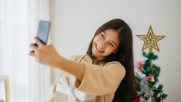 年轻的亚洲女子正在与她的朋友自拍和视频通话。女性在和朋友视频聊天时展示礼盒。新年快乐，感恩节快乐，圣诞快乐图片下载