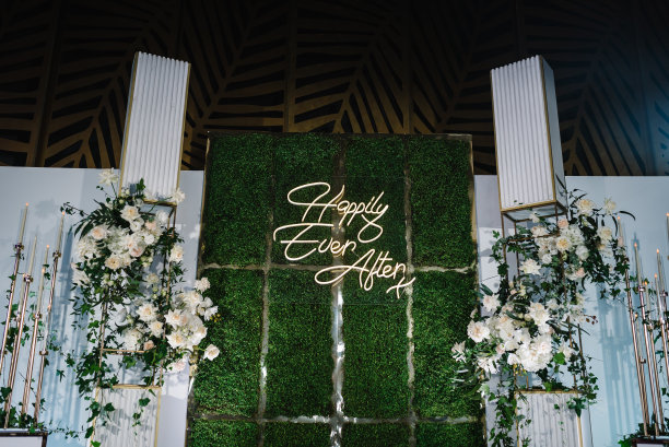 从此幸福地生活在一起。拱门，墙壁，照片区，装饰有白色花朵和绿色植物的区域，大厅里有蜡烛。宴会区域的装饰。奢华仪式中的装饰。图片下载