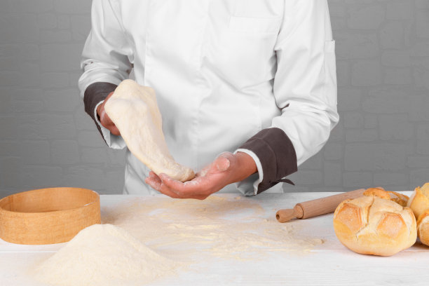 面包师手里拿着面团，旁边是新鲜的意大利小麦面包，白色背景上有面粉图片下载