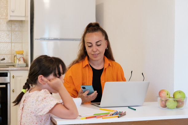 女儿在餐桌上画画，母亲在笔记本电脑前工作图片下载