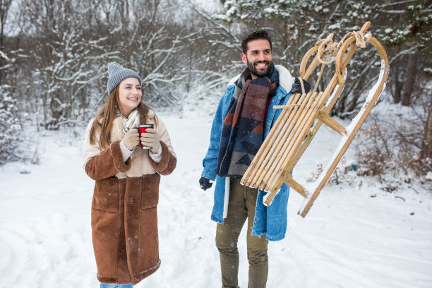 一对年轻夫妇在玩雪球、玩雪橇、喝热饮，享受初雪图片下载